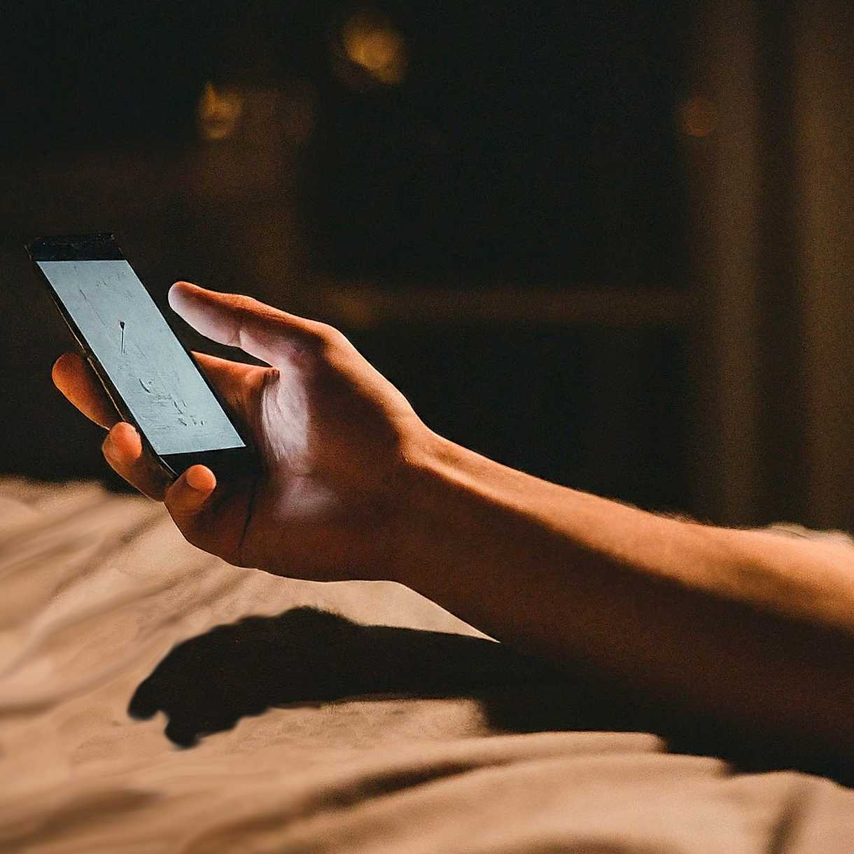 Arm and hand holding smart phone over bed